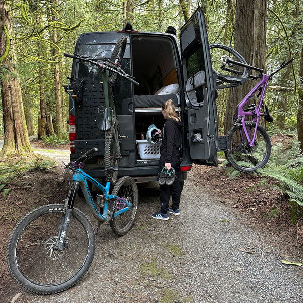 Tokul Racks Sprinter Van with bicycles attached to Panel Bike Rack, person standing next to open van door in a forest setting