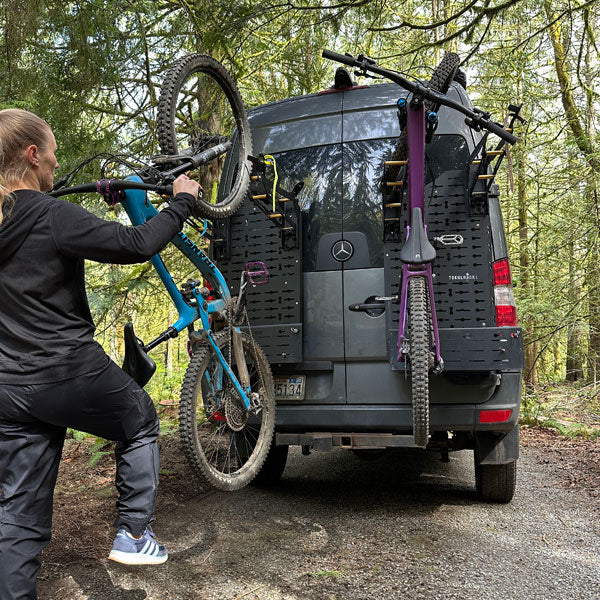Tokul Racks Person loading a bicycle onto Panel Bike Rack on a Sprinter van in a forest setting